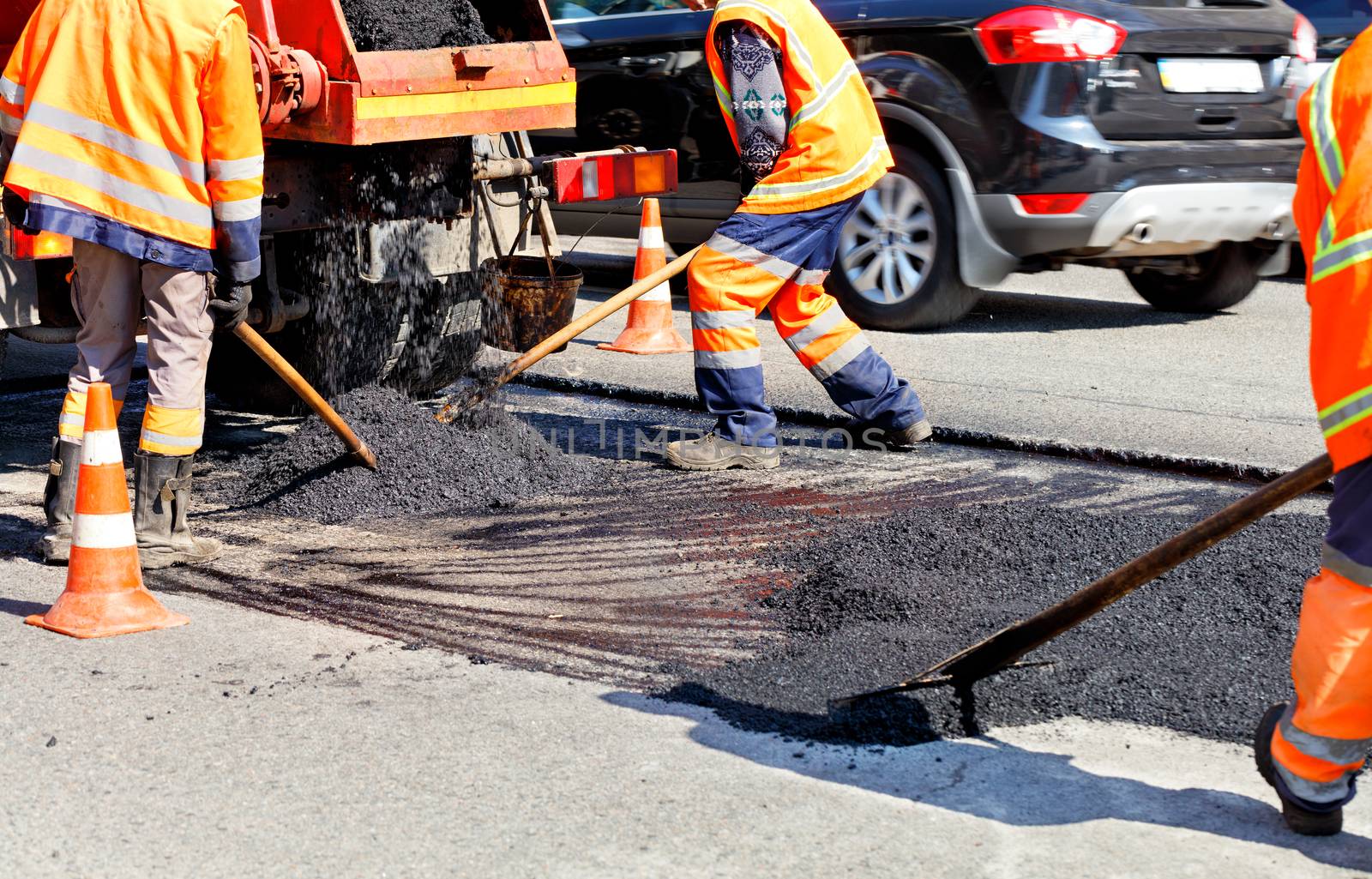 Working team levels the fresh asphalt with shovels on a repaired area in road construction. by Sergii