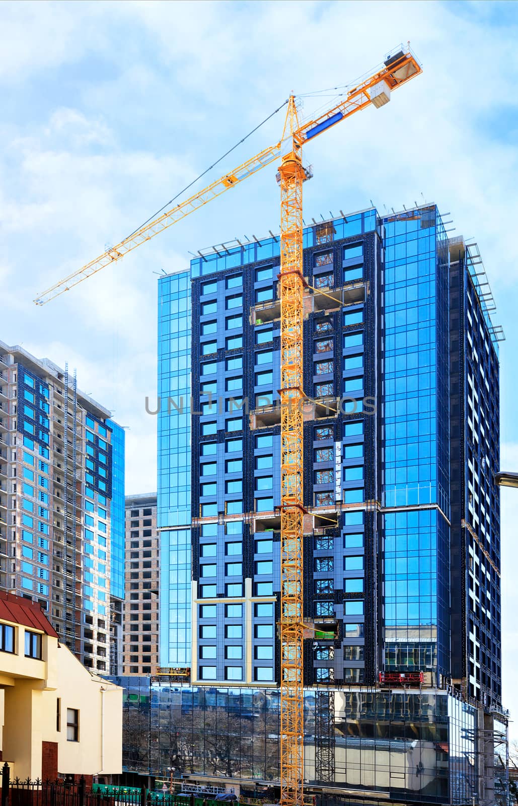 In the construction of modern residential concrete buildings with a glass facade, a tower crane is used, the blue sky is reflected in the windows of the building.