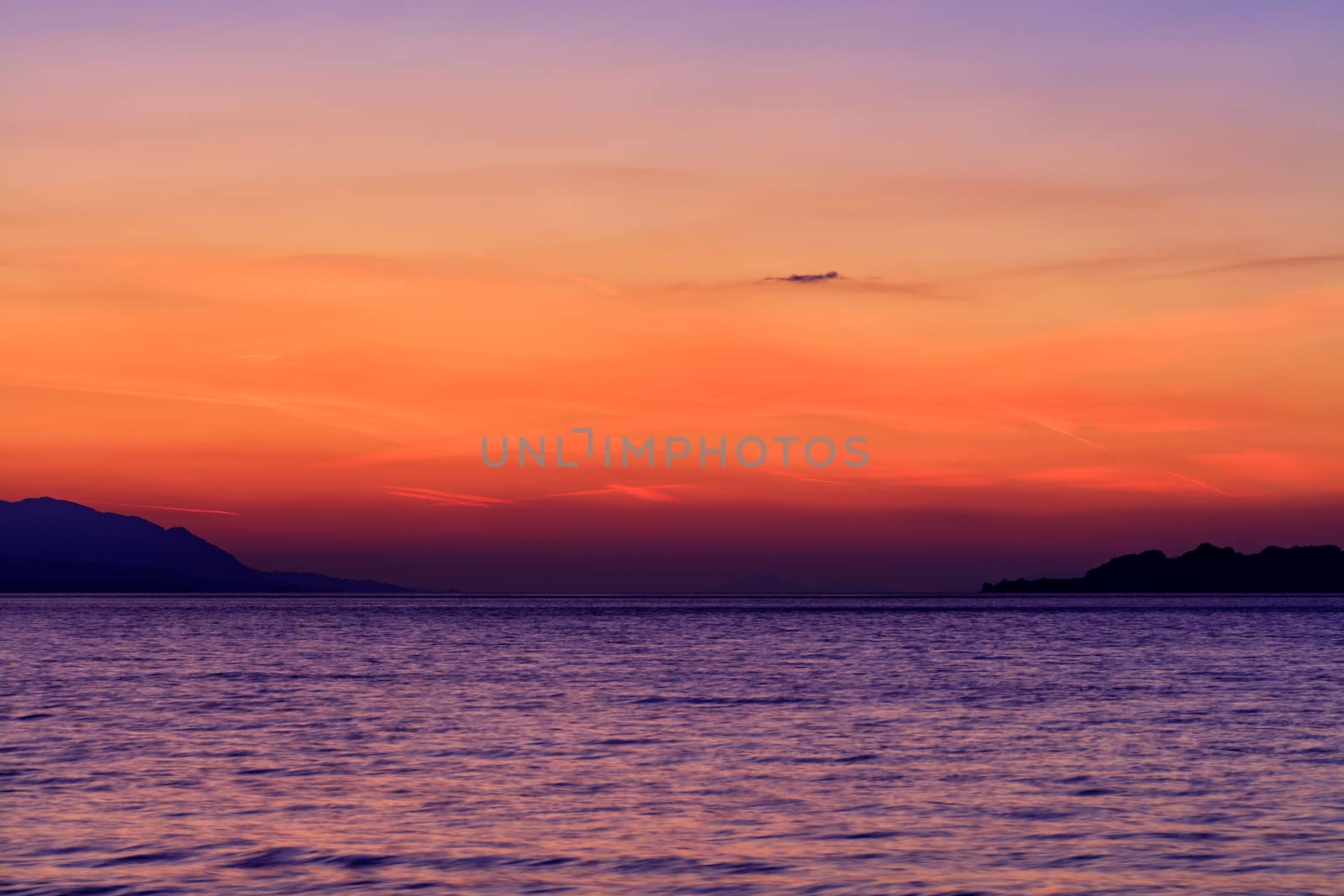 Beautiful, bright sunset on the Gulf of Corinth against the background of the silhouette of the highlands running along the horizon of the sea line. by Sergii