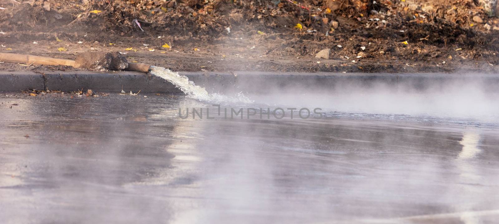 Hot water is pumped out onto the road with a pump and a fire hose, water vapor rises densely above the asphalt, image with copy space.