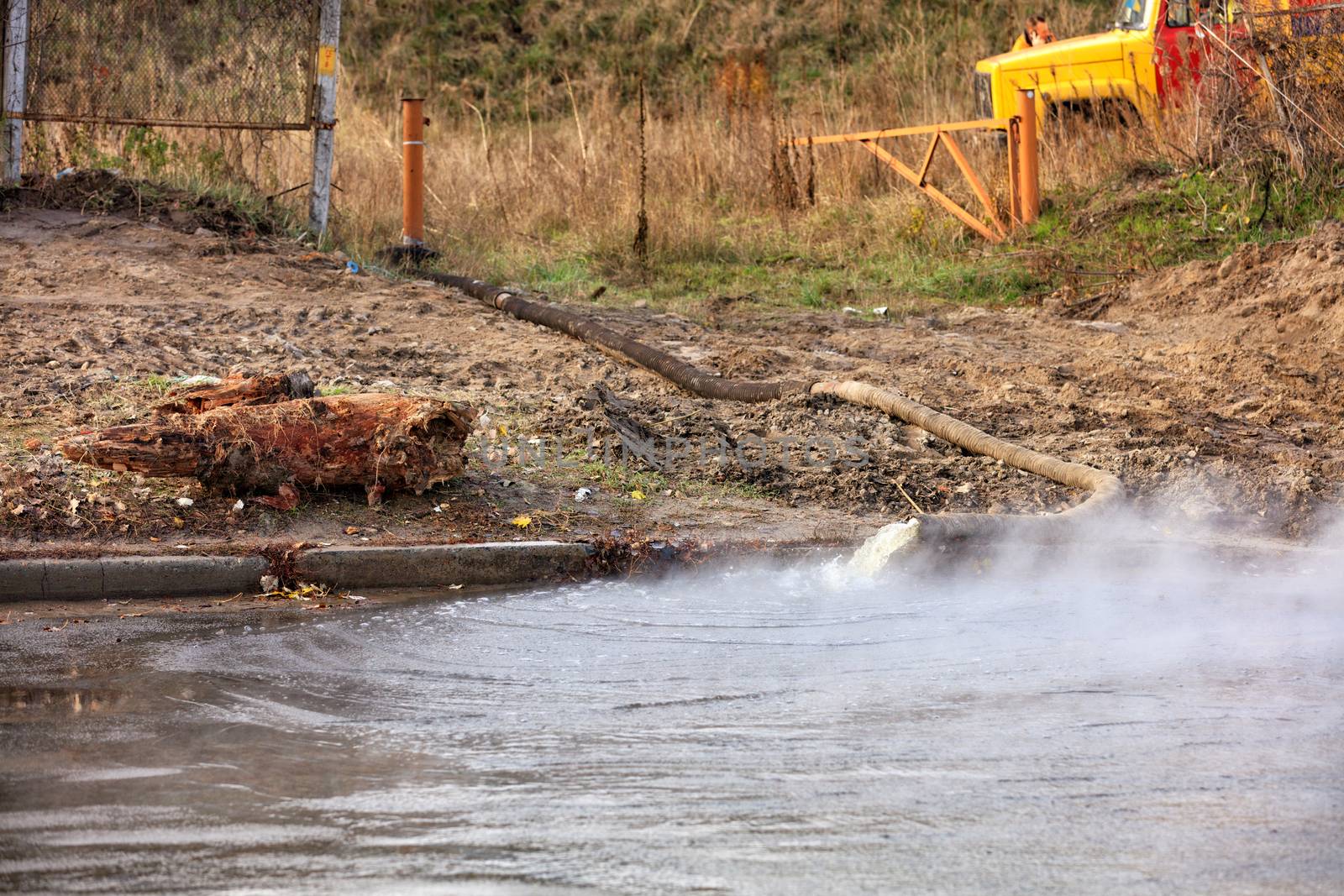 Hot water is pumped out onto the road using a pump and a fire hose from a fire engine, hot water forms a large puddle on the asphalt, water vapor rises tightly over the road, image with copy space.