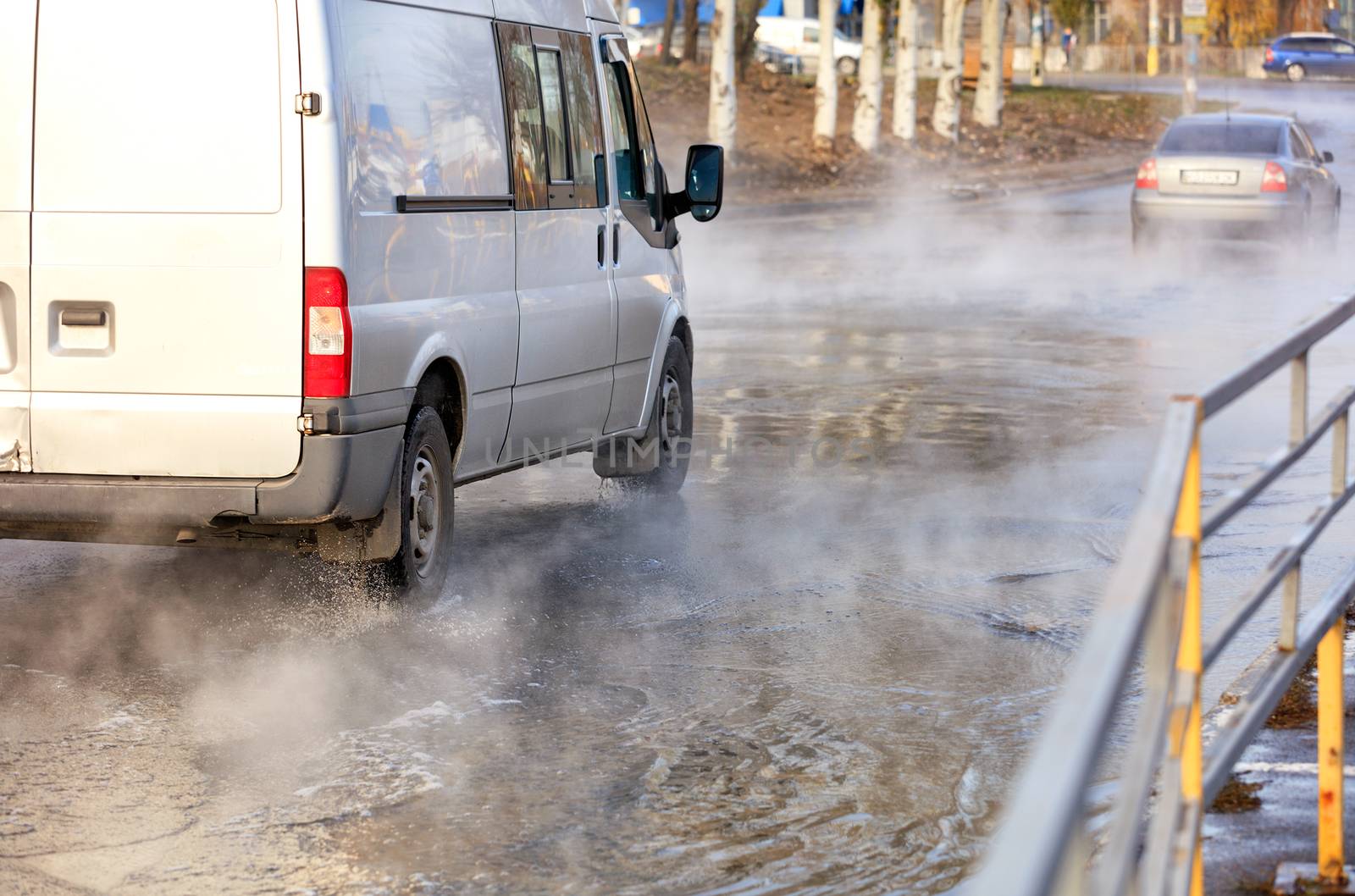 An accident on a heating main, a breakthrough in a pipe with hot water, cars drive along a flooded road, water vapor forms a smokescreen over the asphalt, image with copy space.