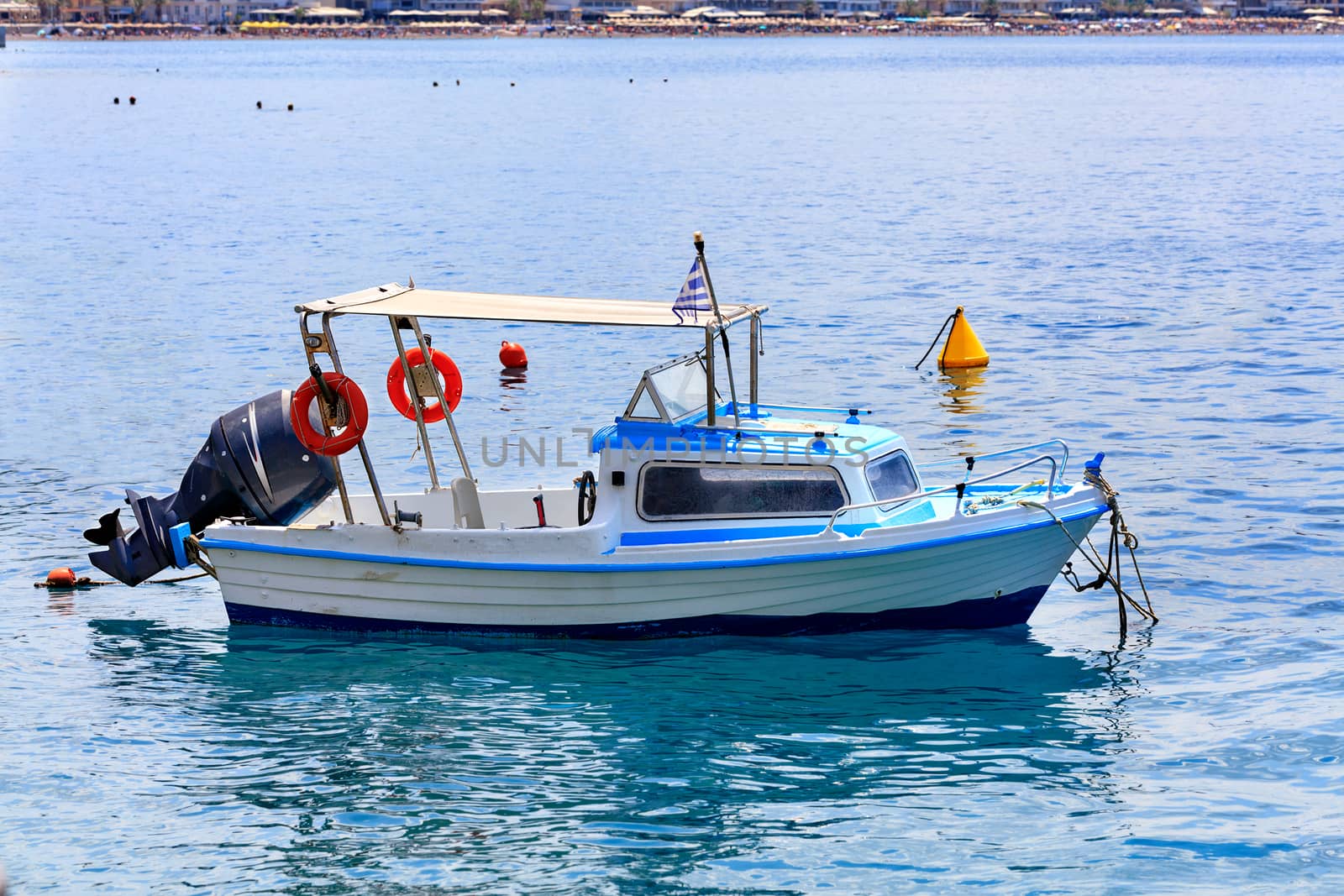A small rescue boat with a powerful motor and orange lifebuoys on board sways on the sea waves of the Greek coast against the background of the beach coastline, image with copy space.