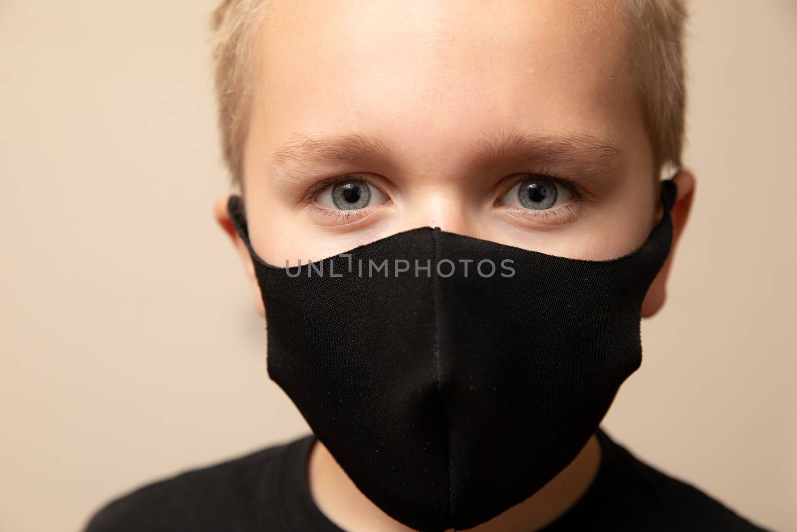 young boy is helping flatten the curve by wearing a black face mask