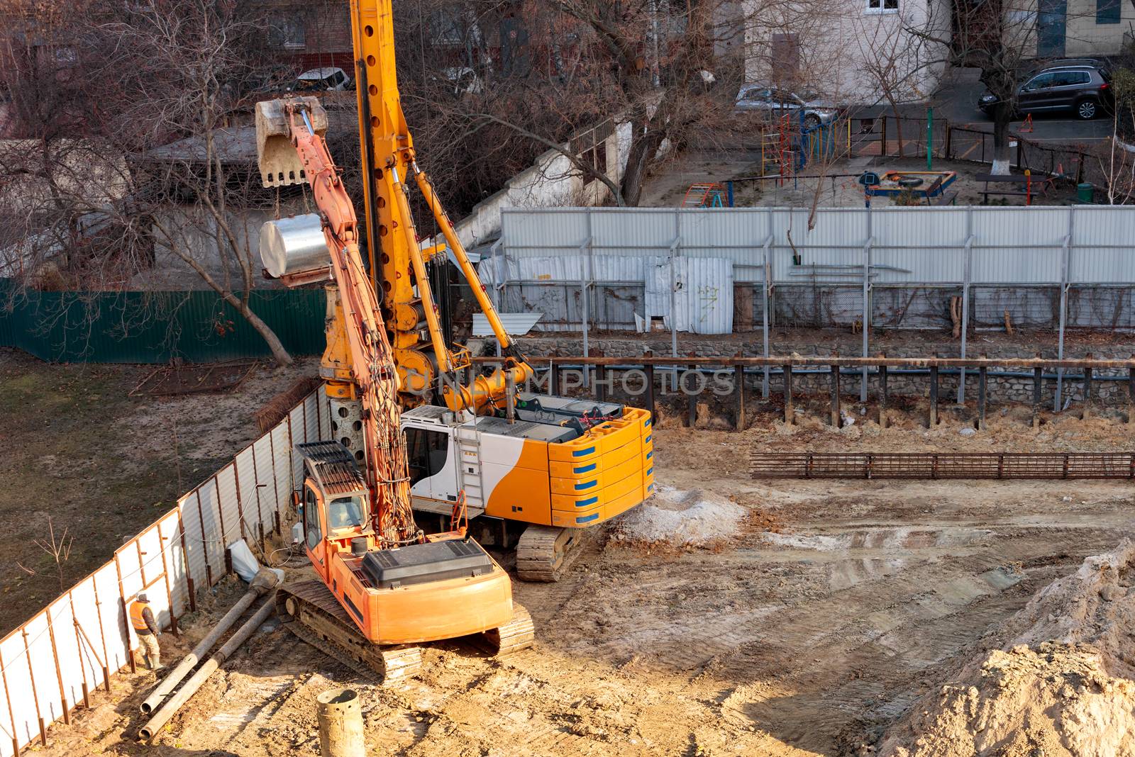 Heavy construction equipment, an excavator and a large powerful crane drill holes in the ground for laying concrete piles in the foundation of the future home, image with copy space.