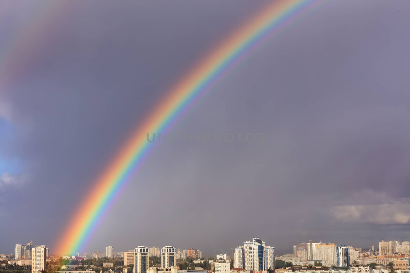 A large bright rainbow in the gray sky above the city after the last thunderstorm. by Sergii