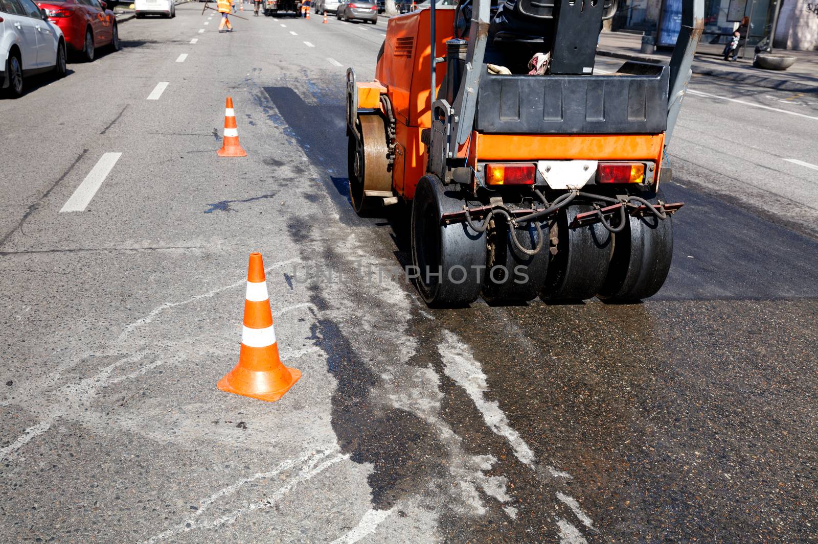 Heavy orange vibrating roller compacts hot asphalt renews a part of the road of the city street, image with copy space.