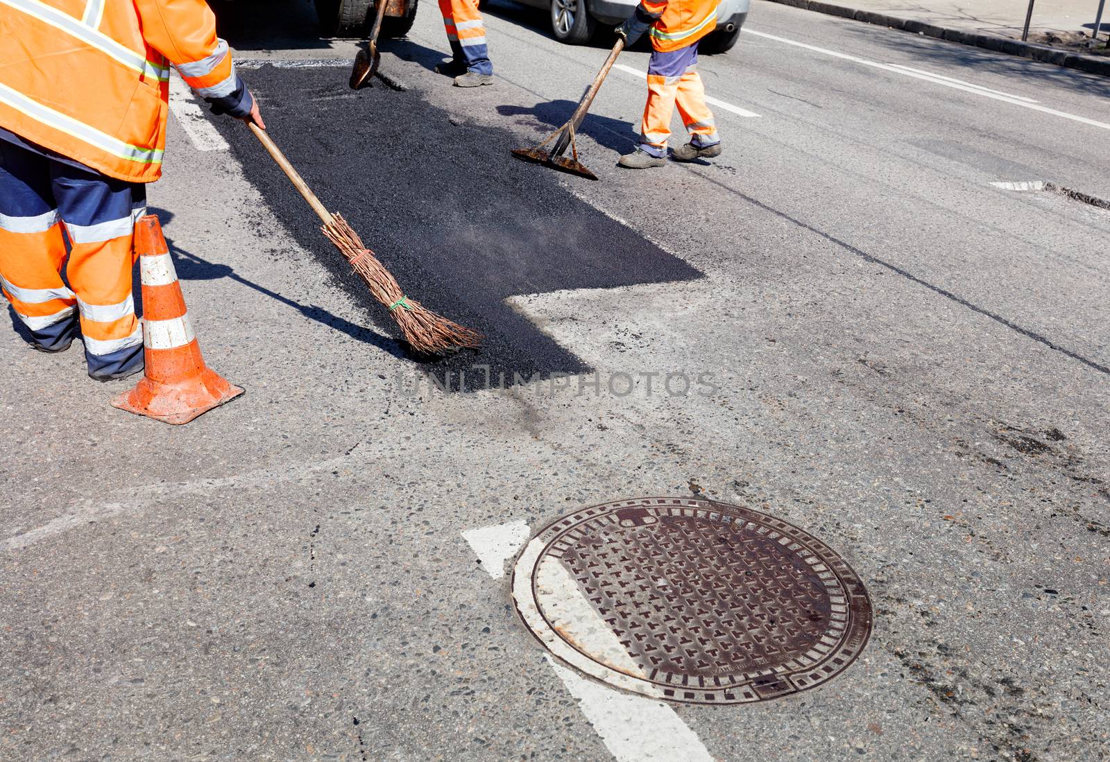 When repairing the road, the working team pours hot asphalt onto even patches with shovels, a level and a broom manually. by Sergii