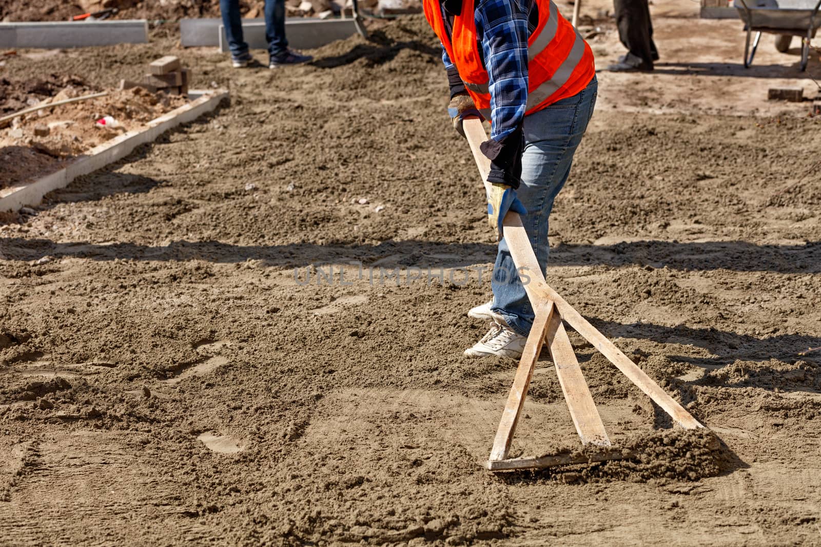 A worker levels the sand base with a wooden level to begin laying paving slabs in the pedestrian area of a city street, image with copy space.