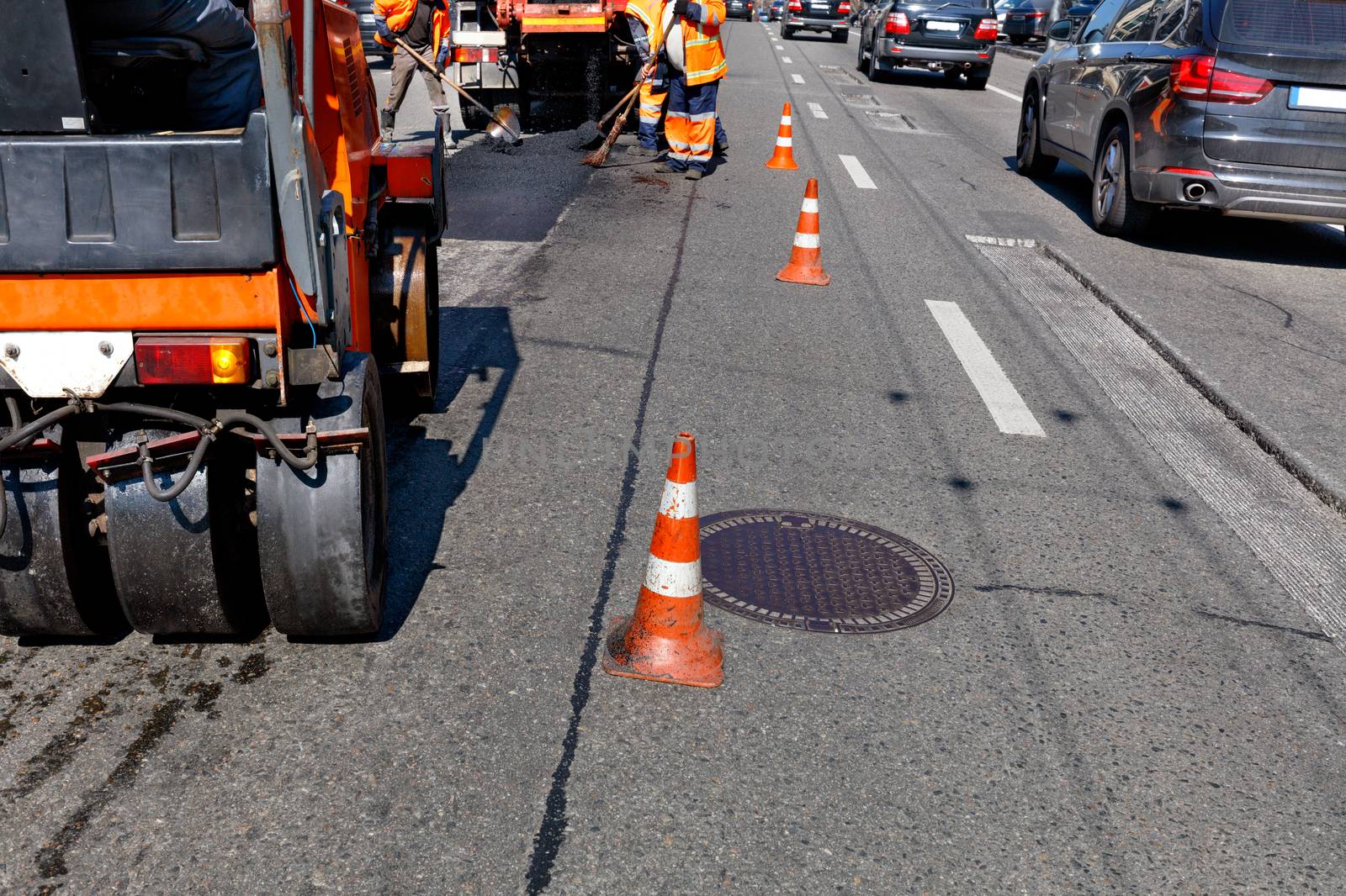 Working team patches the damaged part of the asphalt on the fenced cones stretch of city street, image with copy space.