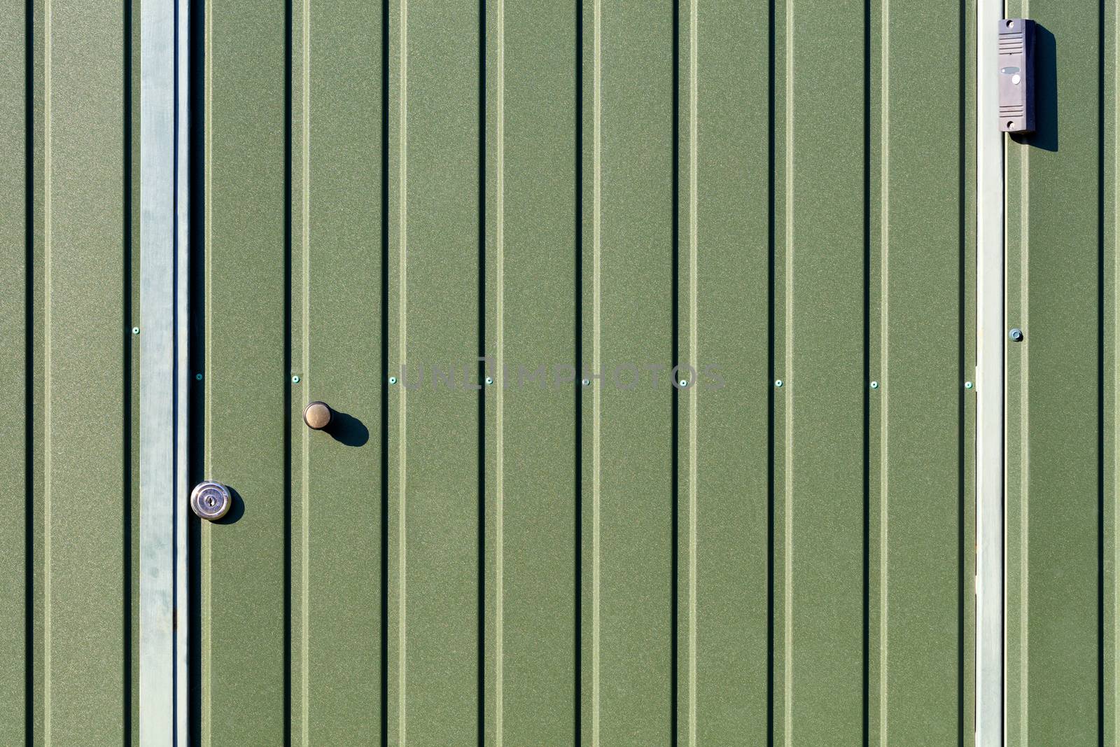 Green metal fence and doors made of corrugated steel sheet with vertical rails and a surveillance camera. by Sergii