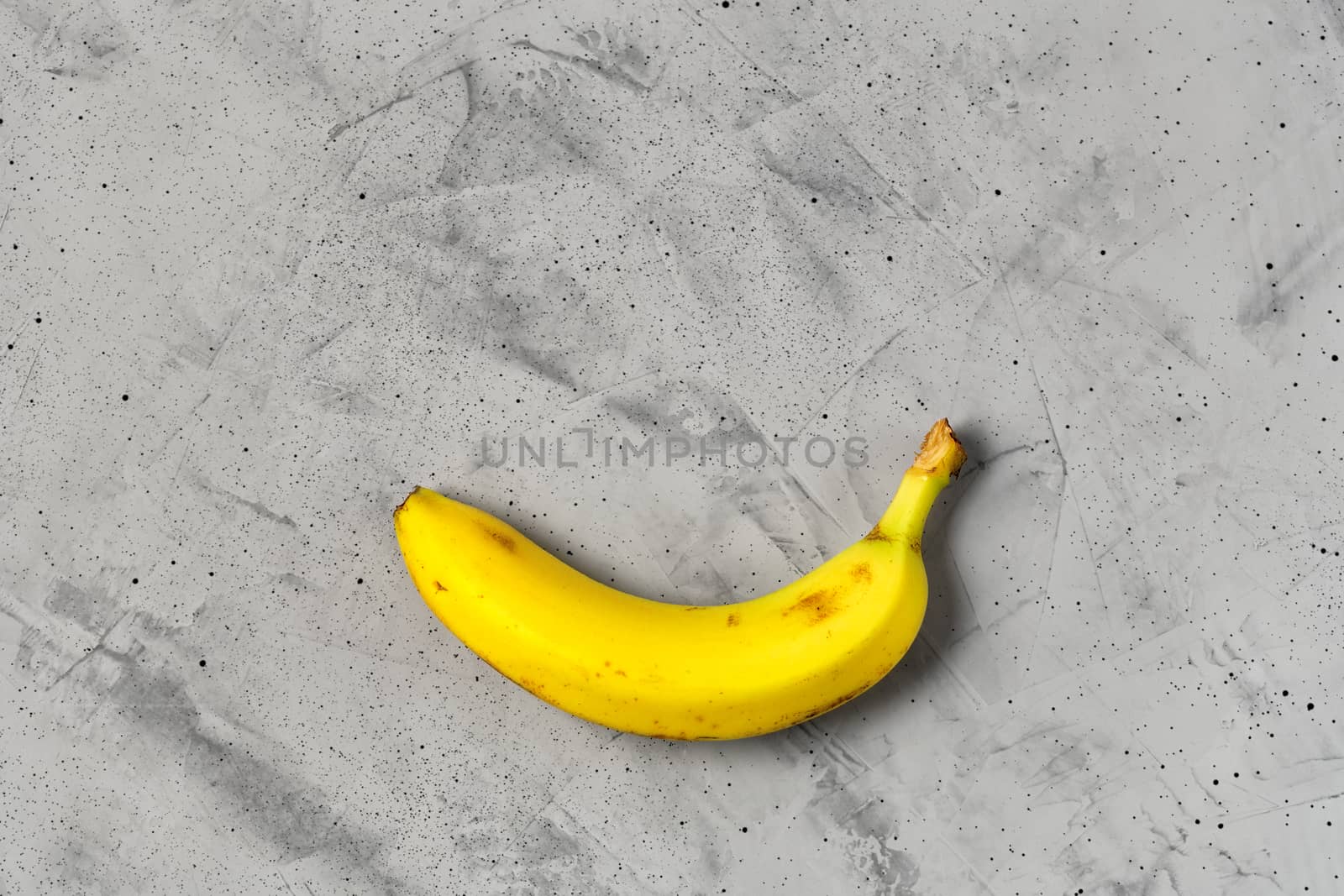 Yellow ripe banana on a gray concrete background, flat lay, image with copy space.