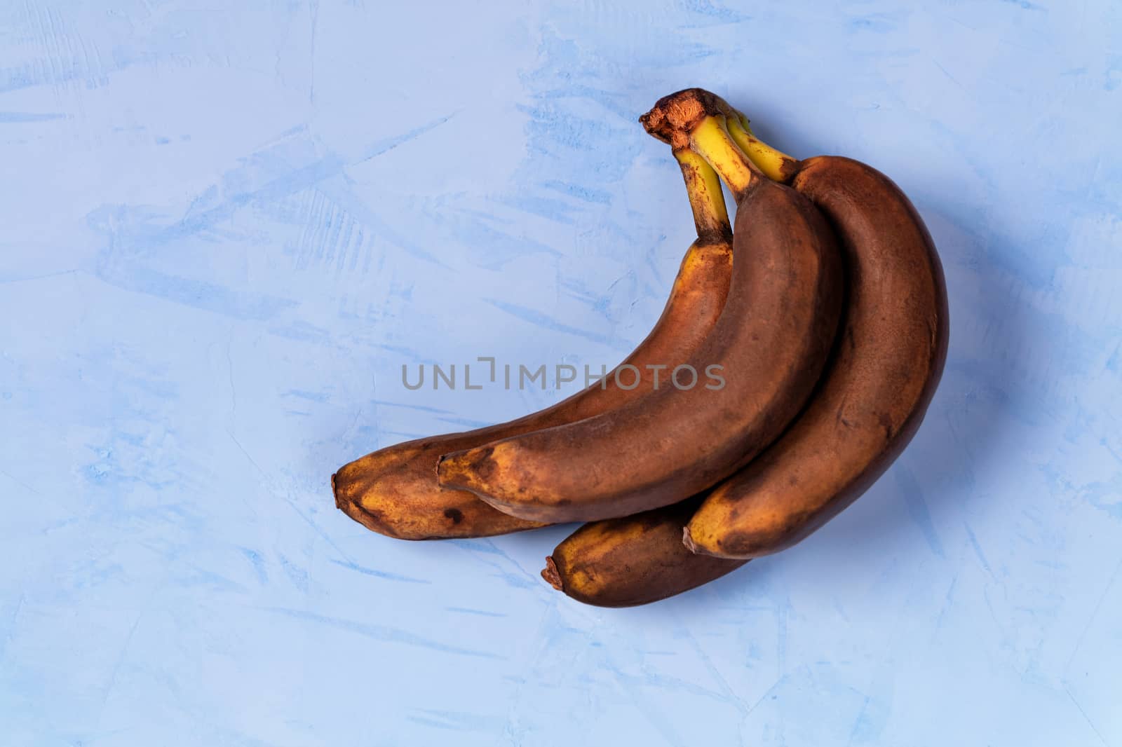 Ugly brown ripe bananas on a background of blue stucco, flat lay, image with copy space.