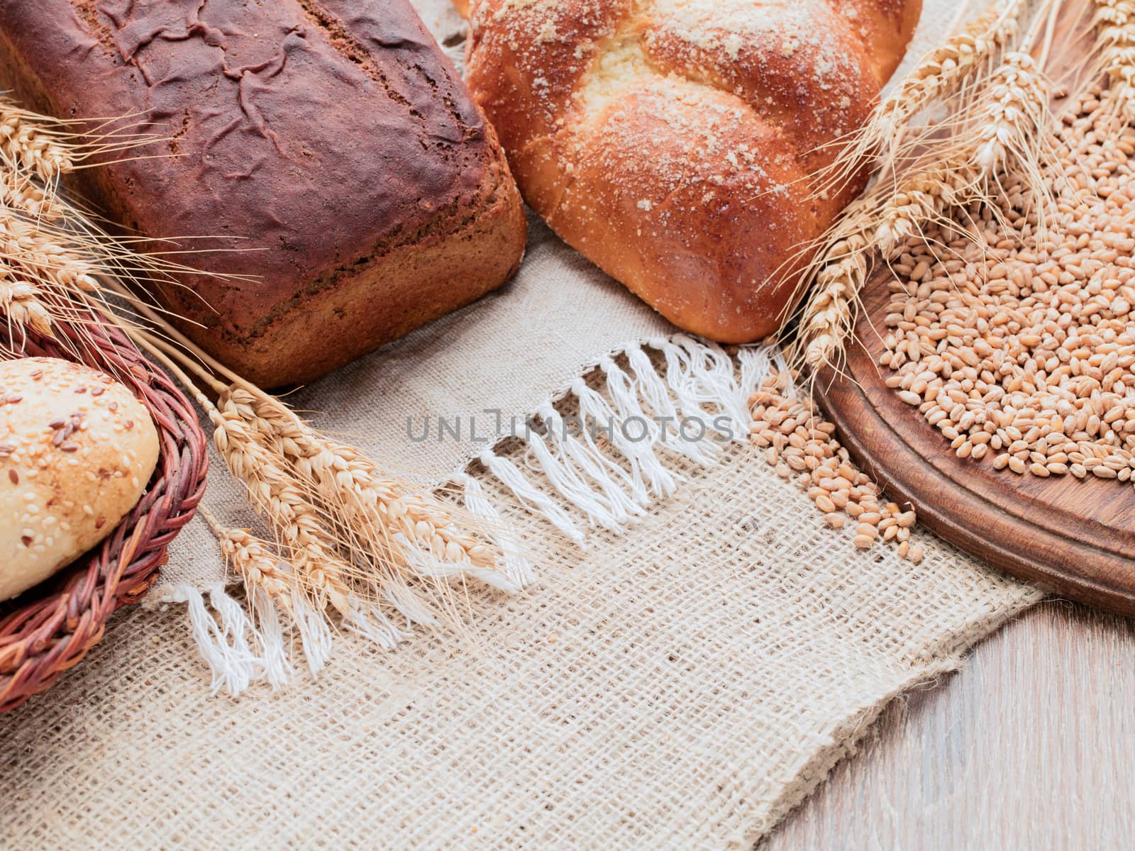 On a wooden table covered with burlap and linen napkins. On a napkin placed rye and wheat bread. Wooden cutting board and basket of bread on a sacking. Ears and grain on a wooden cutting board.