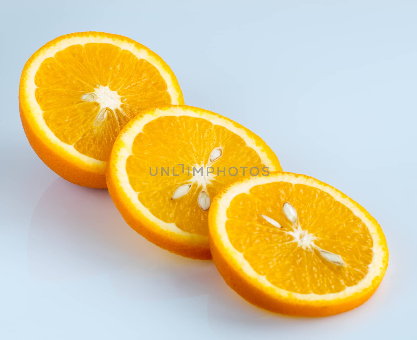 Three rings of sliced juicy ripe orange on a light blue background.