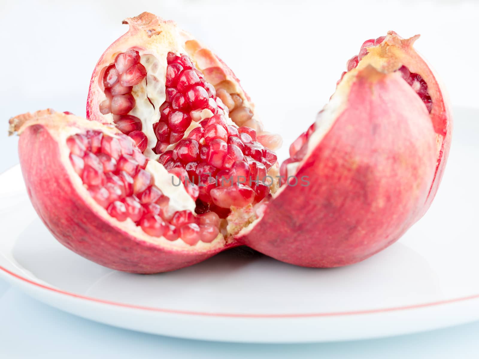 Ripe pomegranate fruit on a white porcelain plate by Sergii