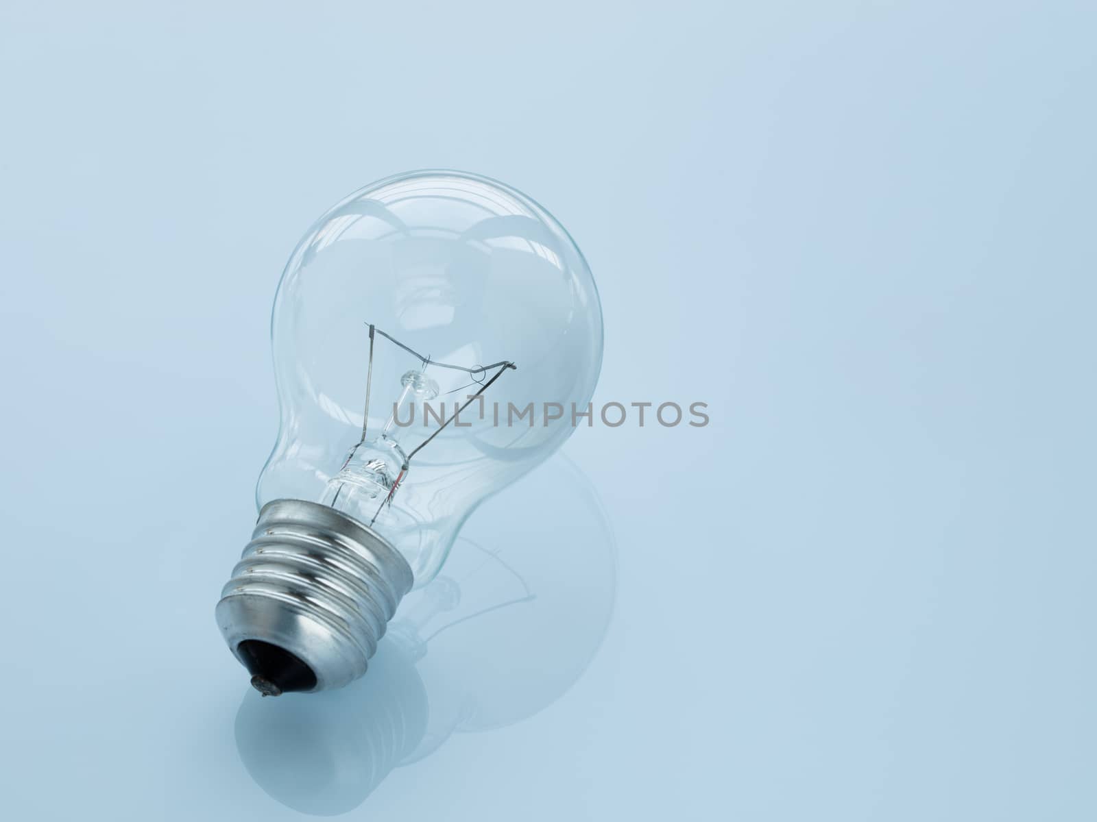 The light bulb lies on a glossy surface on a light blue background. Reflection of a light bulb.