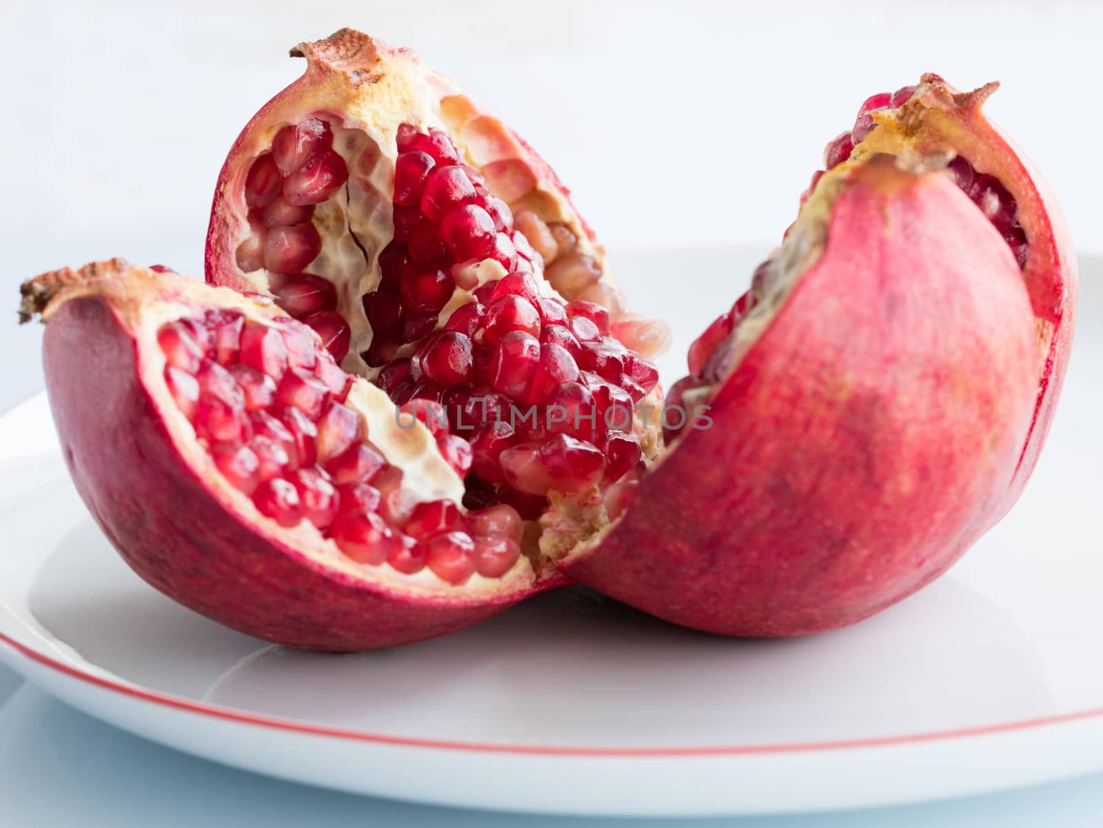 The Ripe pomegranate fruit and broken into four parts, on a white porcelain plate. The plate with a pomegranate border.