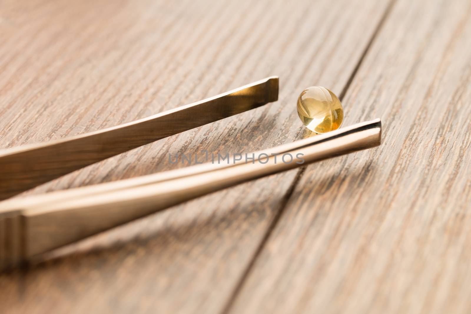Fish oil pill in tweezer on wooden table background