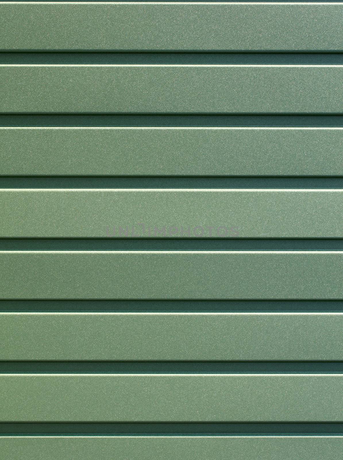 Greenery metallic fence made of corrugated steel sheet with vertical guides. Corrugated green iron sheet background close up.