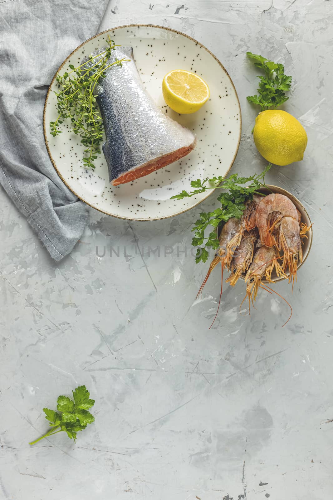 Trout fish  surrounded parsley, lemon, shrimp, prawn in ceramic plate. Light gray concrete table surface. Healthy seafood background.