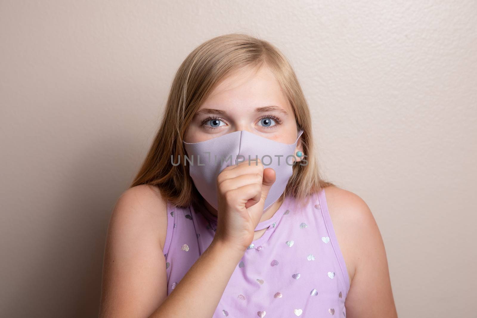 Straight on image of a girl coughing using her hand and a face mask