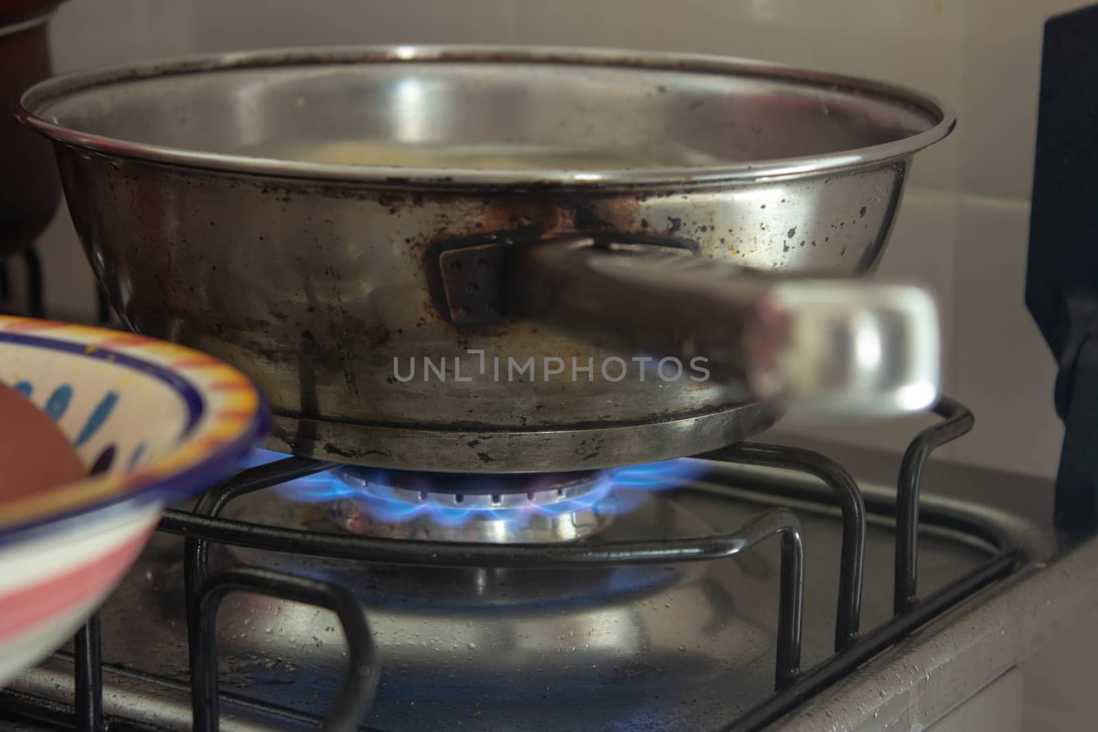 Iron pan boiling some water with pasta on a stove with the fire on