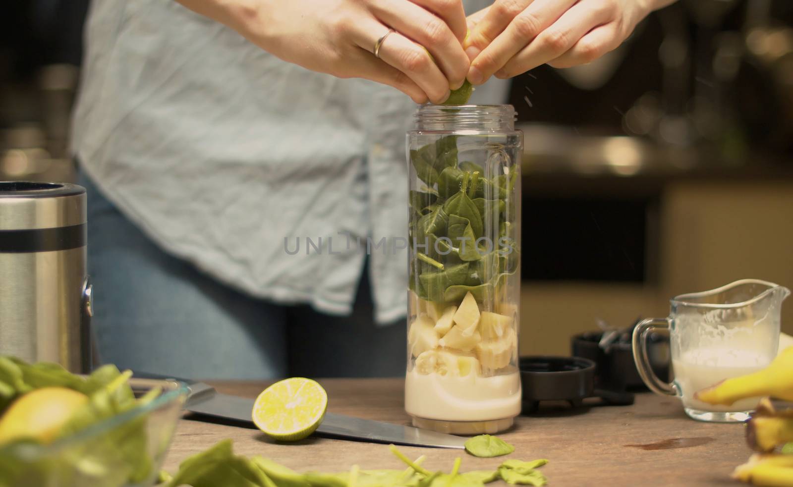 Female hands squeezing lime juice into a blender glass with smoothie ingredients. Cooking smoothies in the kitchen. Healthy lifestyle and eating concept