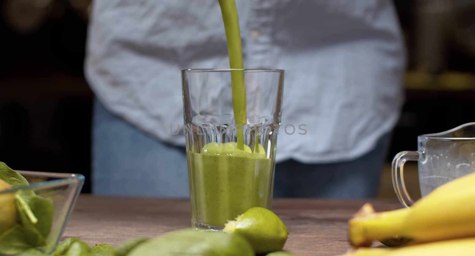 Close up pouring into a glass green banana spinach smoothie. Healthy lifestyle and eating concept