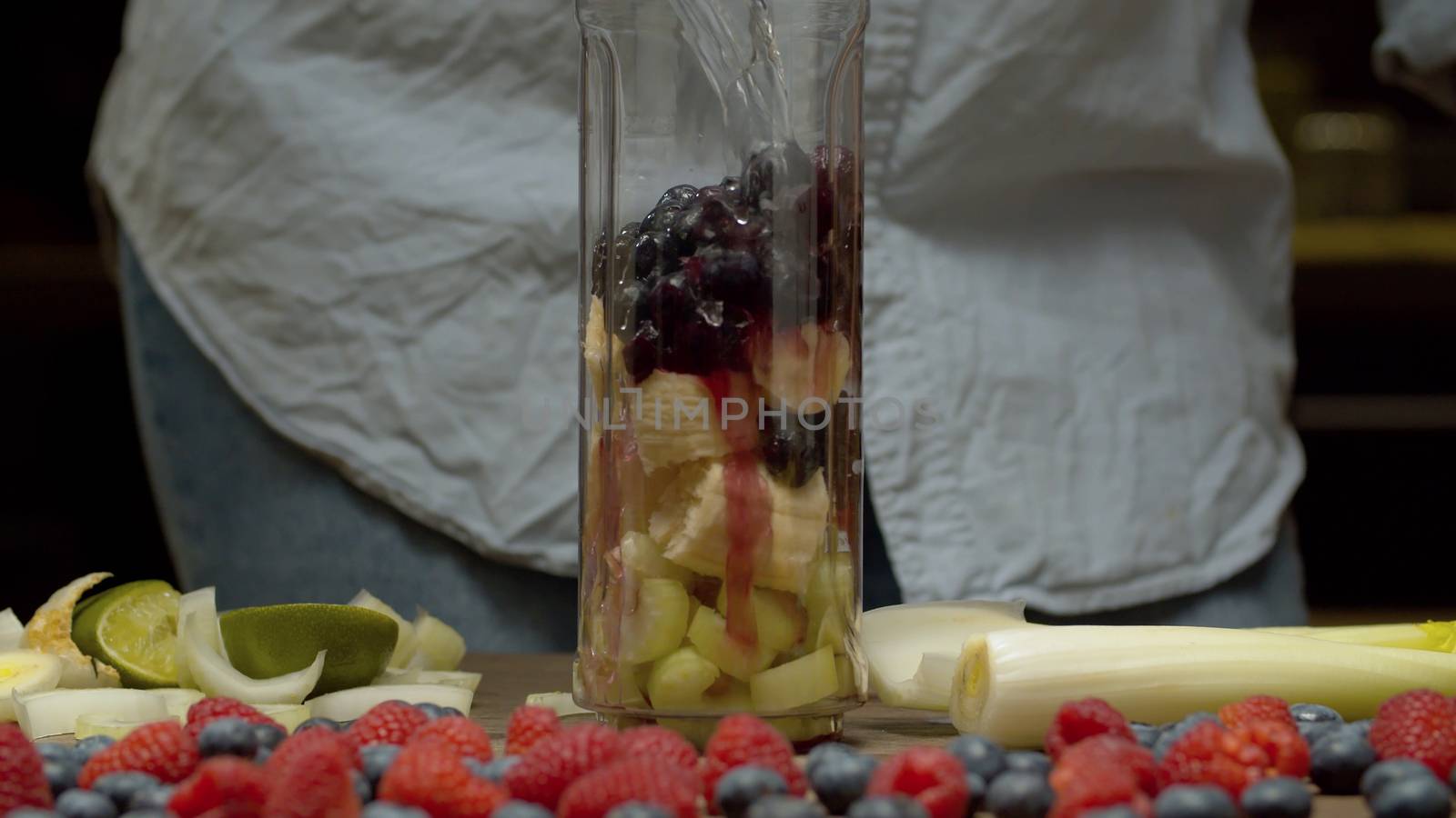 Close up pouring water in blender glass with banana, blackberry and celery slices. Fresh healthy food