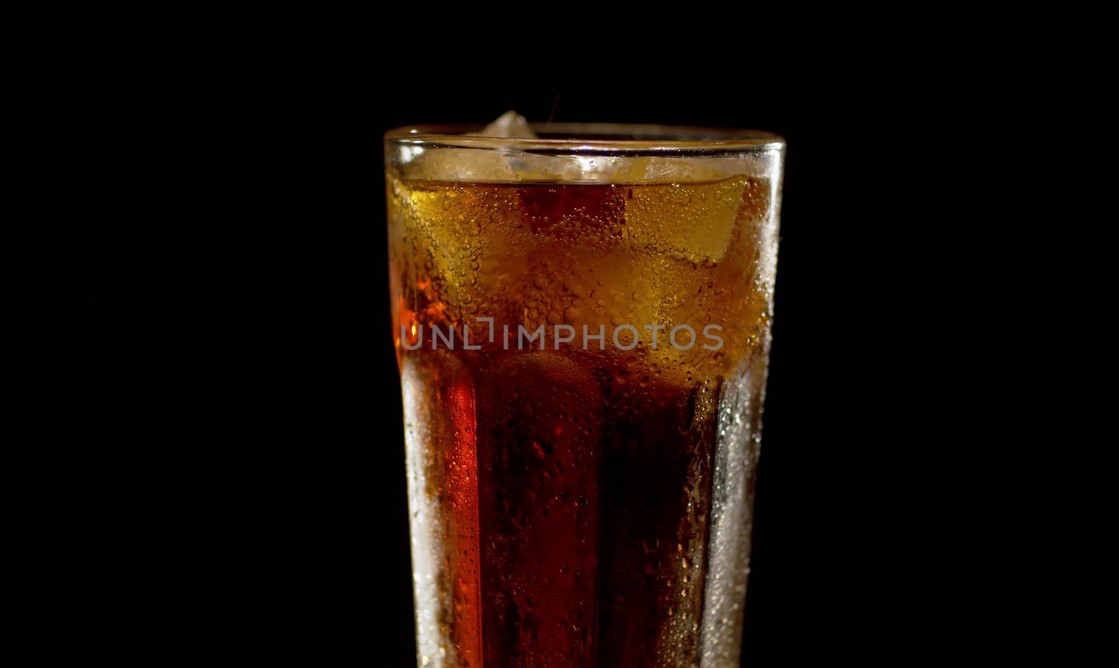 Close up full misted glass of cold cola with ice on black background. Bubbles on ice and water droplets on the glass. Closeup fizzy drink