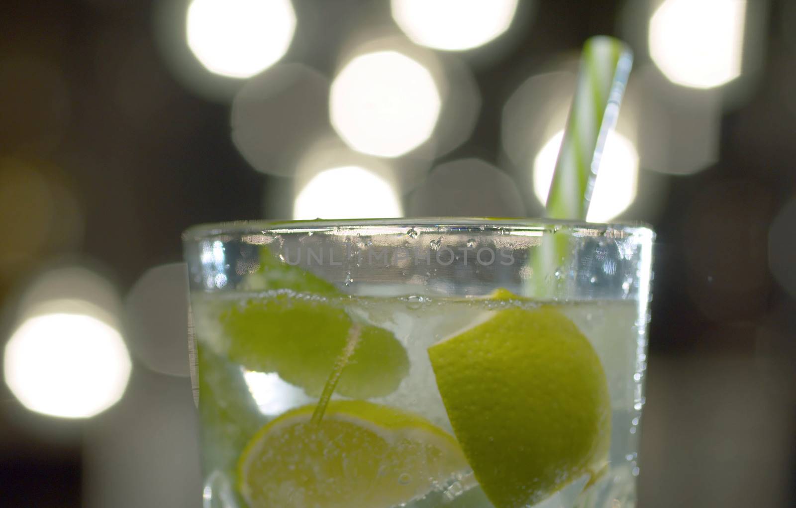 Close up glass of sparkling water with mint, lime and ice on a blurry lights background