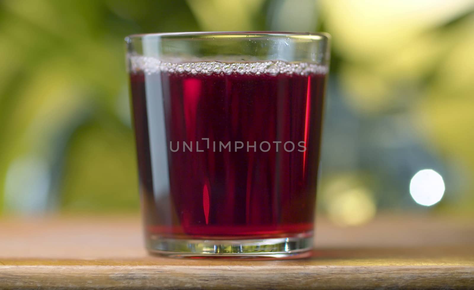 Red transparent juice or wine in the glass against natural green background. Close up cherry or pomegranate or cranberry juice or wine. Healthy eating concept.