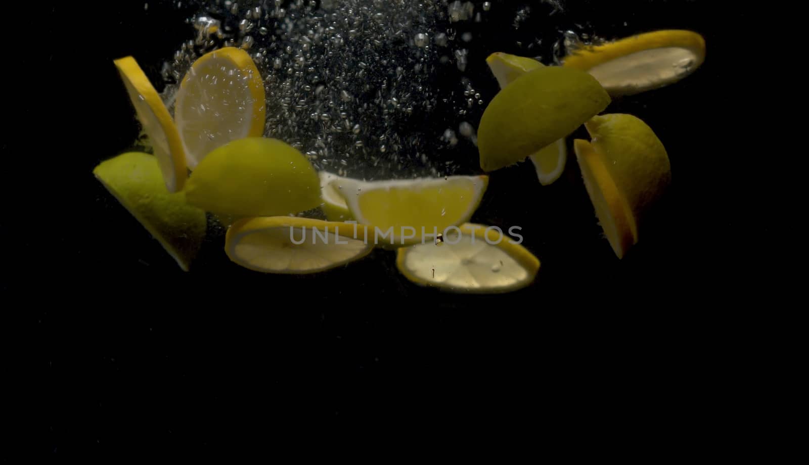 Close up sliced fresh lemons falling into the water on black background