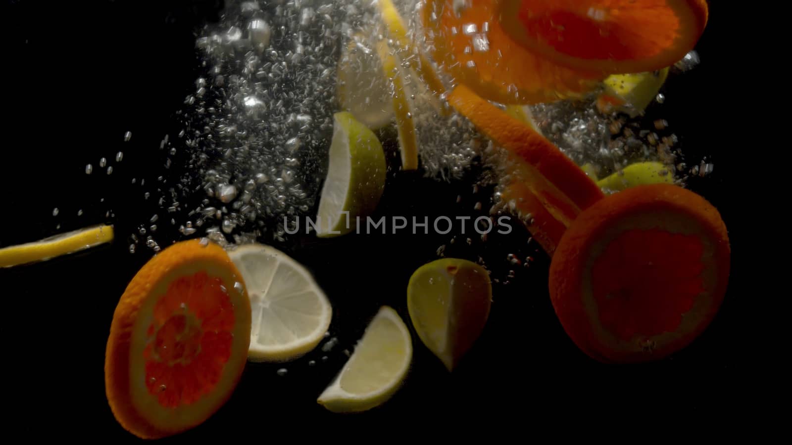 Close up sliced fresh lemons and oranges falling into the water on black background