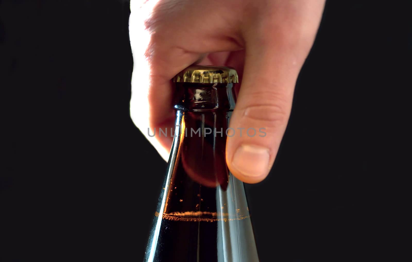 Close up man's hand opening a bottle of beer, side view, black background.