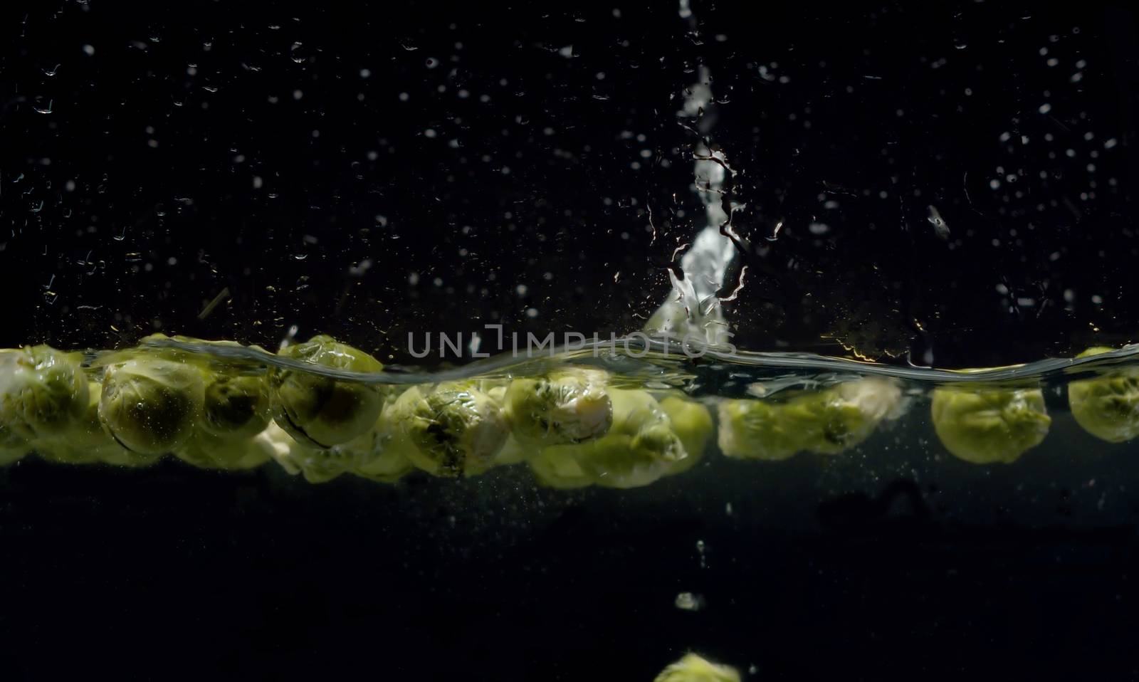 Close up brussels sprouts falling into the water with a splash and bubbles on black background