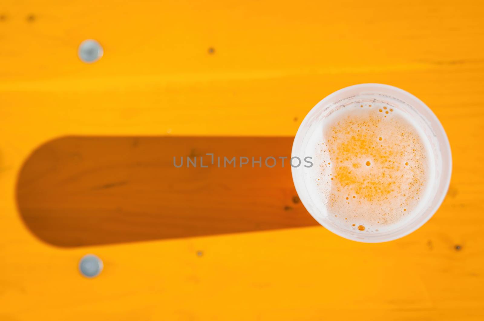 Cold beer in a plastic glass on a wooden bench with lateral sunset light