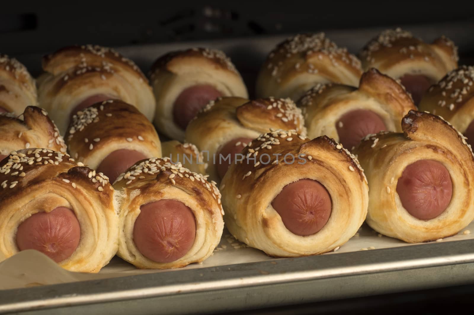 Baked sausages in dough with sesame on the baking tray. Fresh homemade bakery.