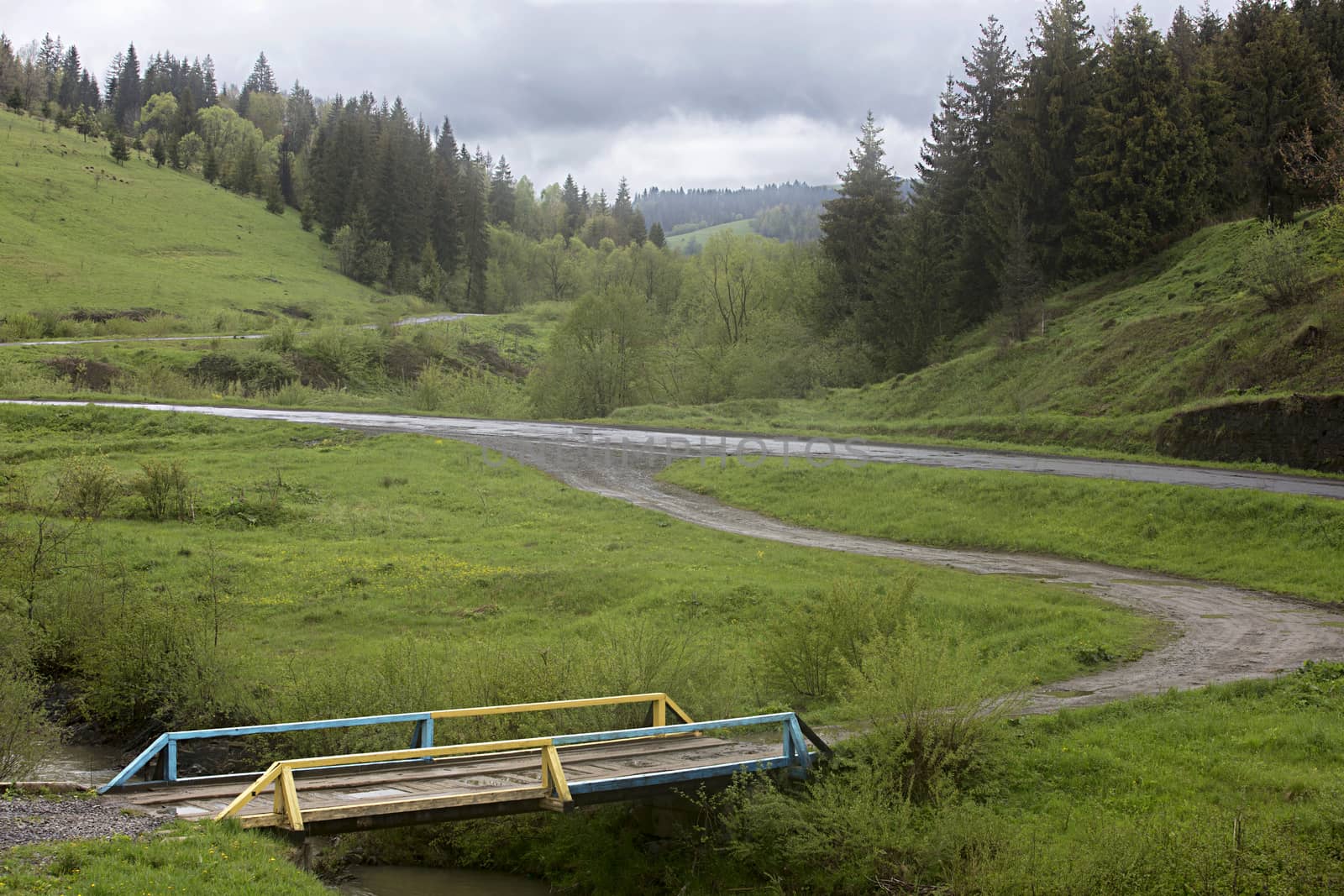 A wooden old bridge over a stream in the valley of the mountain Carpathian road, passing between the hills.