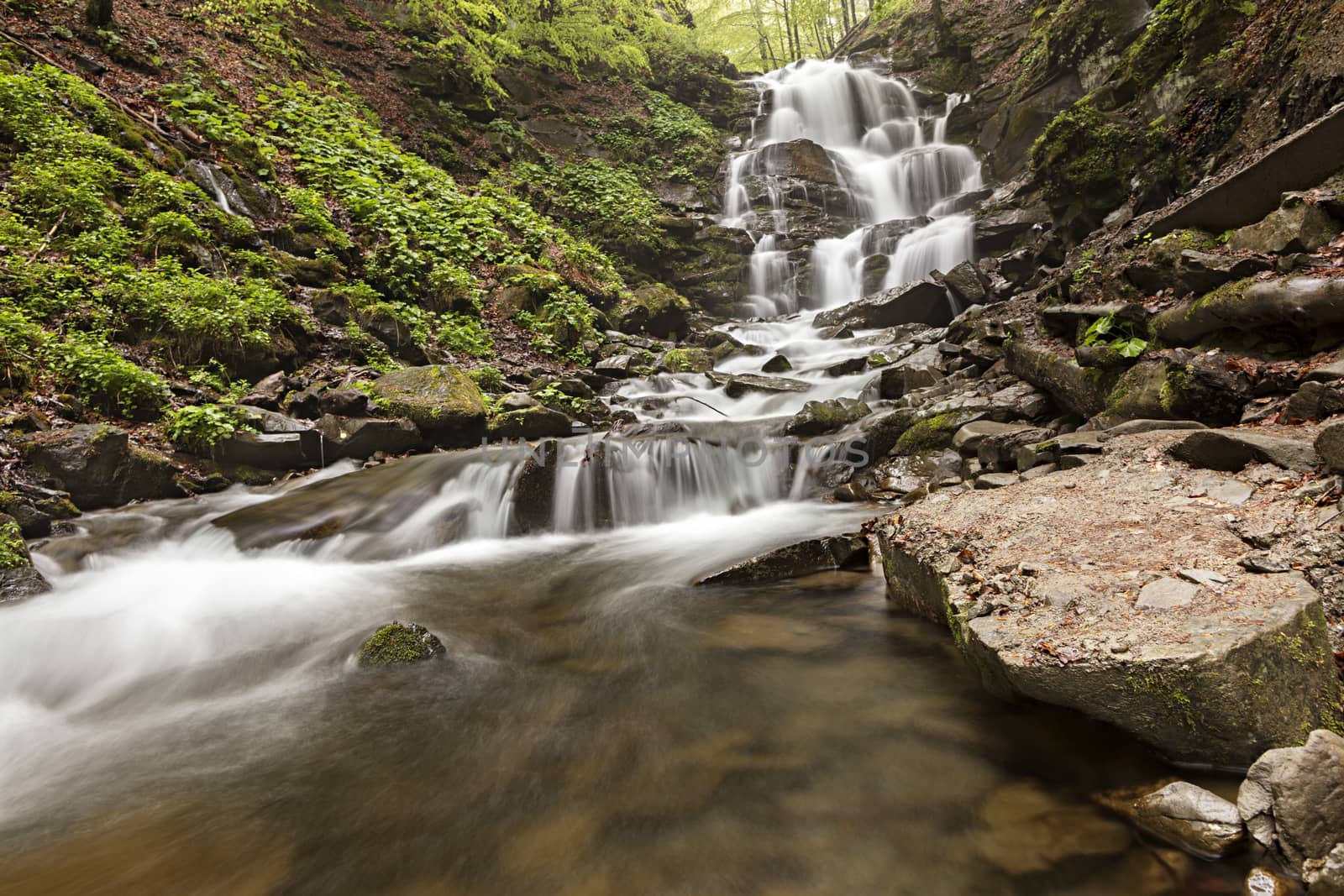 A large boulder washed early in the morning at the foot of a waterfall in the Carpathian Mountains