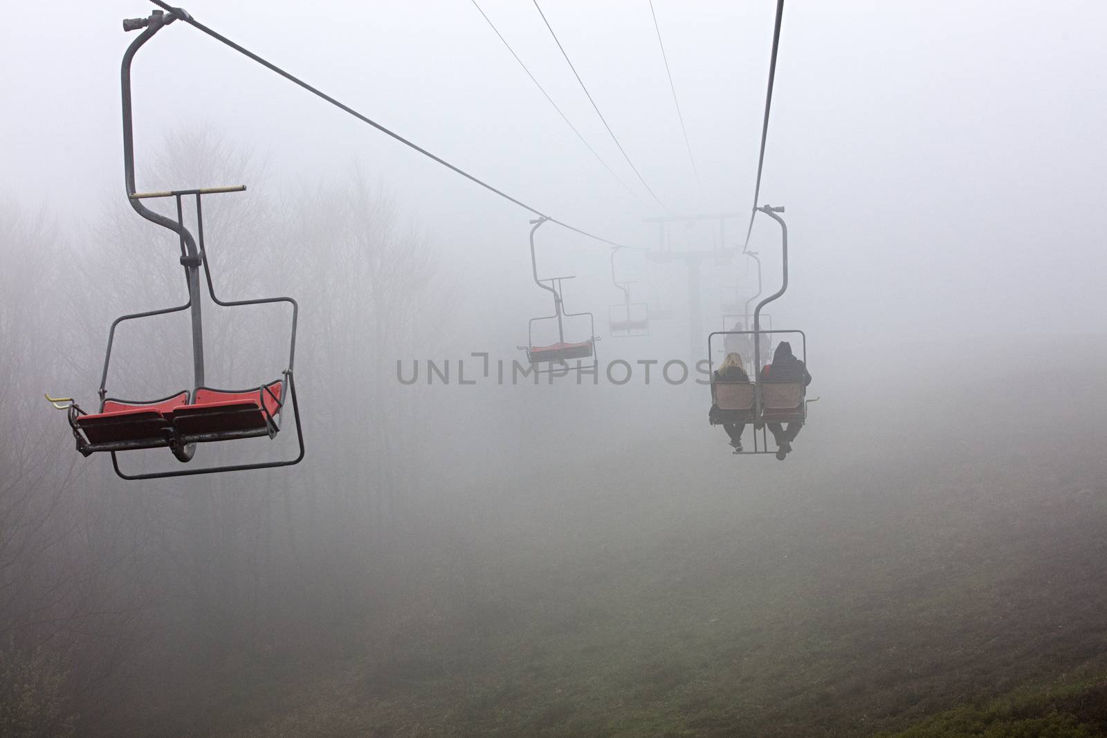 Early in the morning, a mountain lift takes tourists to a sleeping mountain, enveloped in a very dense fog