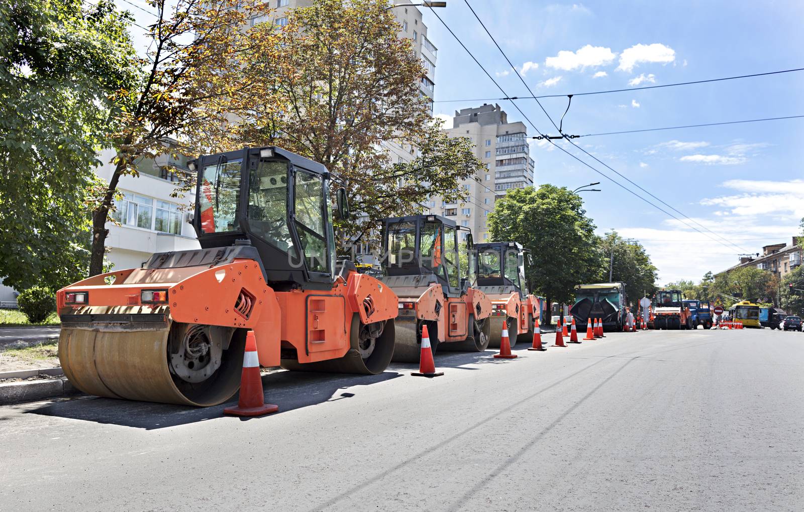 Among the summer noon three heavy road vibrating roller compactors and other equipment are ready for repair of the road in a modern city