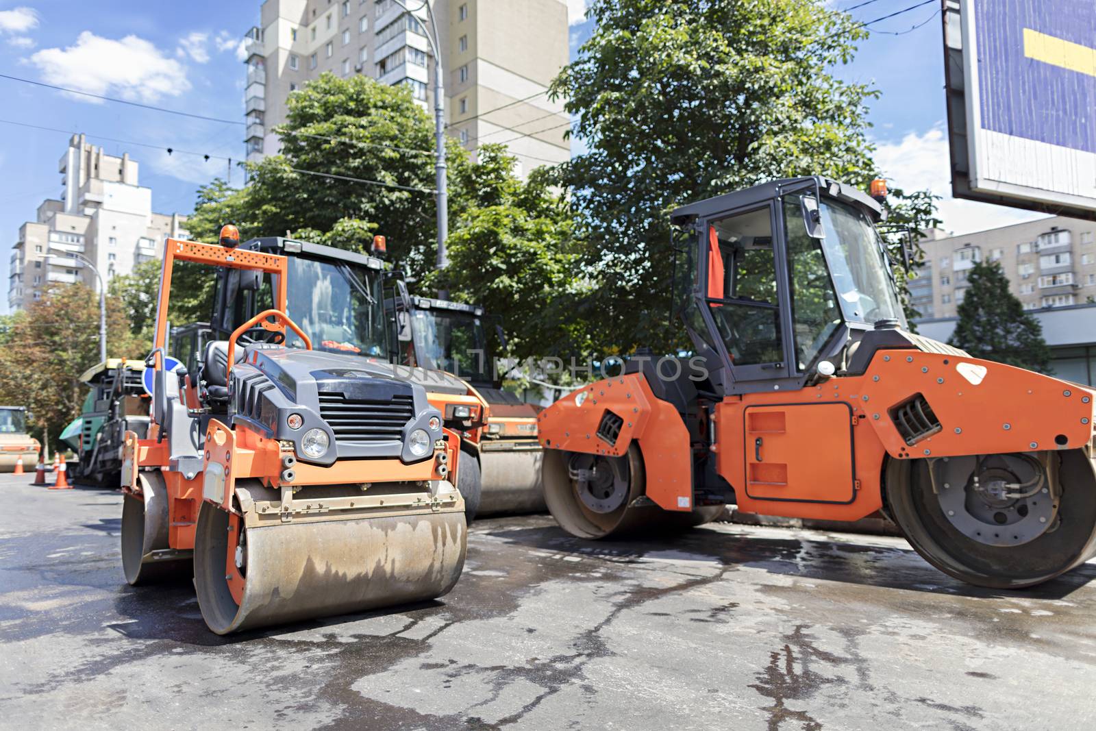 Among the summer noon five heavy road vibrating roller compactors and other equipment are ready for repair of the road in a modern city