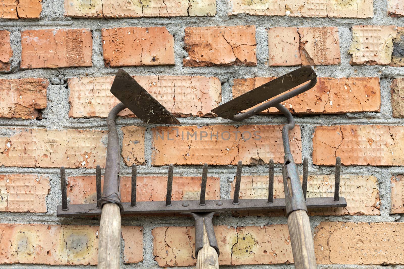 Still life of old / rusty, rake and hoe garden tools against the old weathered brick background making horizontal lines.