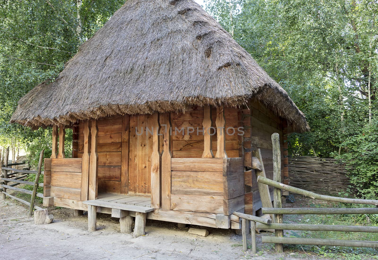Old traditional Ukrainian rural barn with a thatched roof and a wooden, wicker fence around it in a green garden