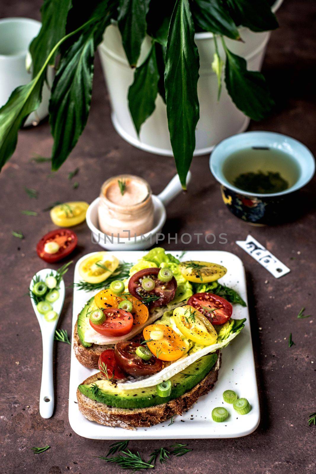 Avocado and tomato toast with salt and pepper over a withe plate and tea and plants in the background