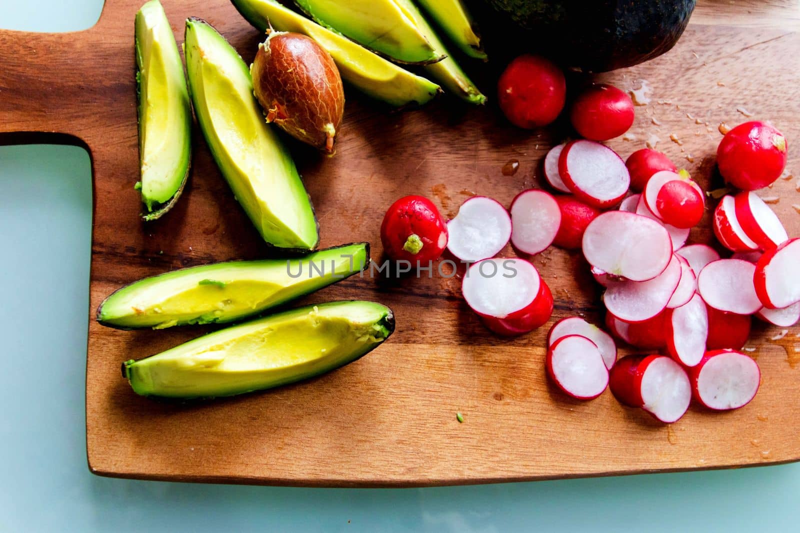 Sliced avocado and radish on a wooden chopping board
