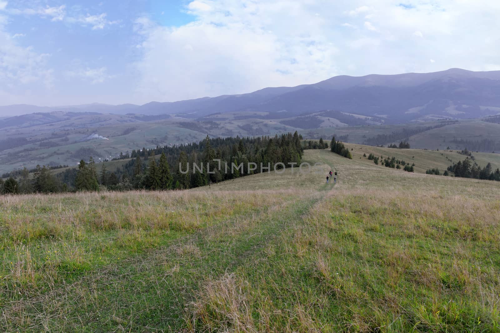 The road at the top of the mountain along which a group of tourists descends down on the background of a mountain summer landscape.