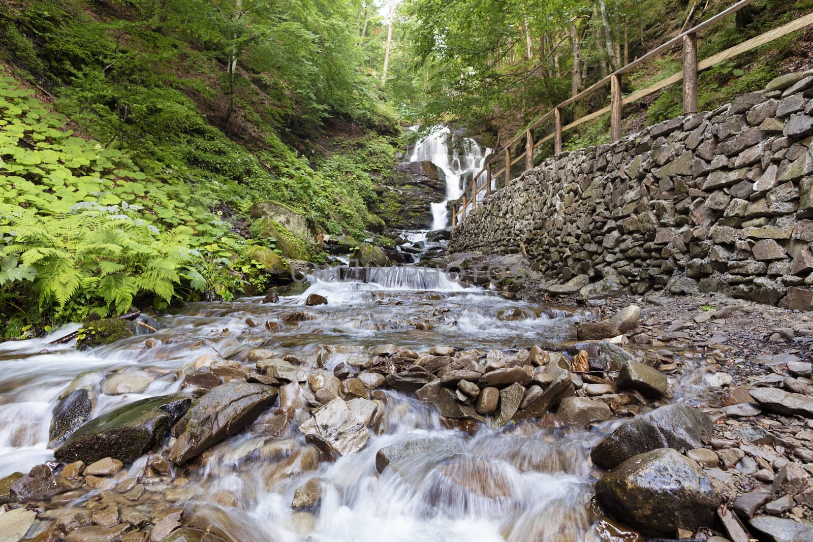 Stone path along the waterfall Shipit between the green overgrown hills in the Ukrainian Carpathians